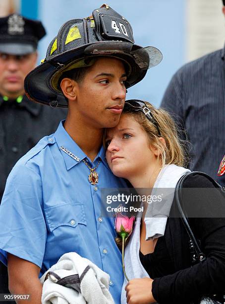 Child wearing a firefighter's uniform comforts a young woman as family members pay their respects at Ground Zero during a 9/11 memorial ceremony on...