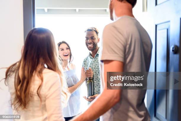 couple greeting friends bringing wine bottle at door - door greeting stock pictures, royalty-free photos & images