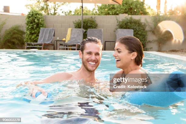 smiling caucasian couple relaxing in swimming pool - man on float stock pictures, royalty-free photos & images