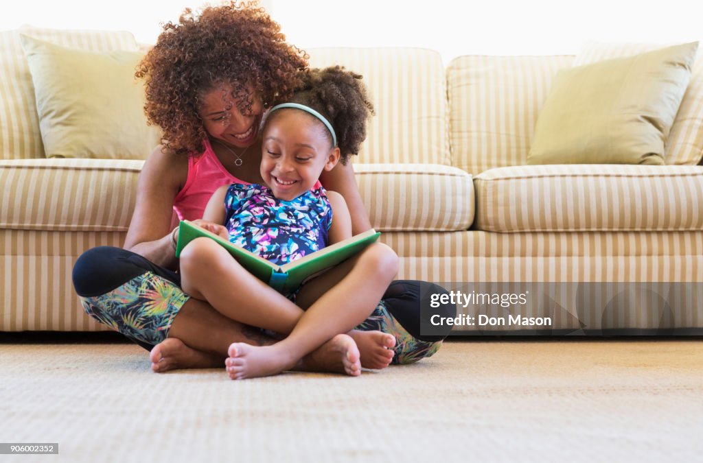 Mixed race mother and daughter reading book on floor near sofa