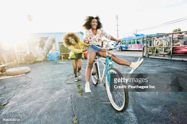 friend pushing carefree woman on bicycle - friends cycling stock pictures, royalty-free photos & images