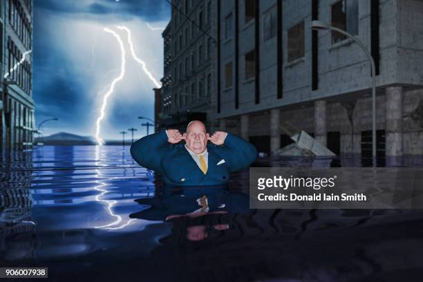 overweight businessman with fingers in ears in flooded city - natural disaster photos et images de collection