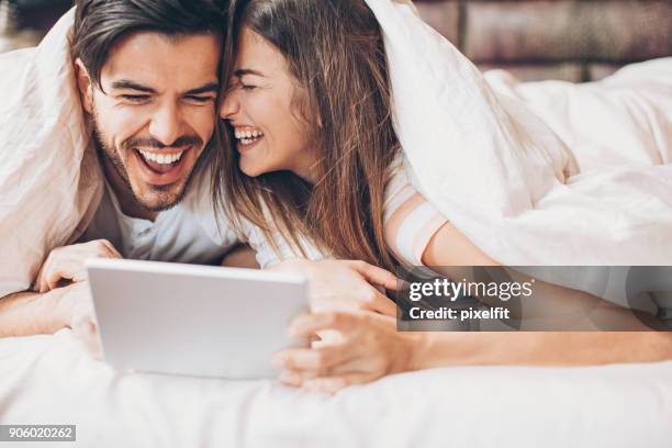 ベッドでデジタル タブレットとの楽しみを持っているカップル - couple under sheets ストックフォトと画像