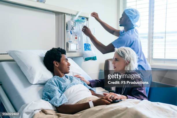 doctor comforting boy laying in hospital bed - man and woman holding hands profile stockfoto's en -beelden
