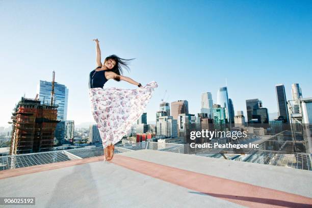 asian woman jumping on urban rooftop - trying on ストックフォトと画像