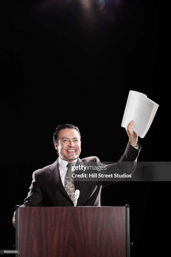 Hispanic man holding document up at podium