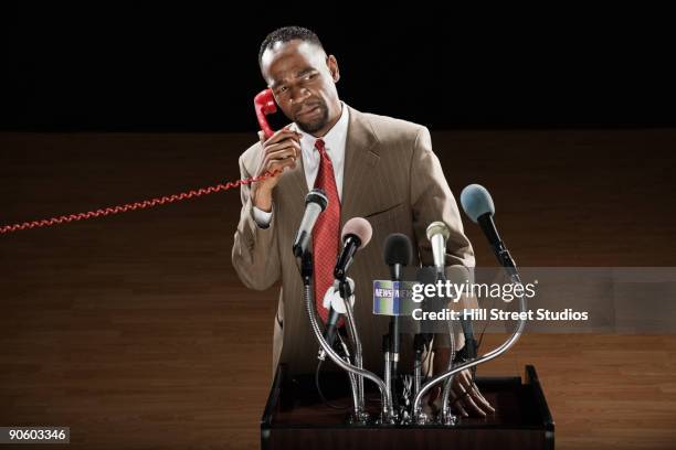 african man talking on telephone at podium with microphones - mike storen stockfoto's en -beelden