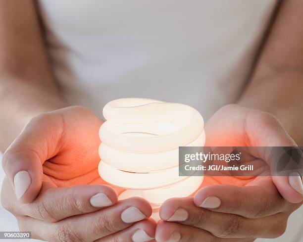 woman holding glowing compact fluorescent bulb - afl woman stock-fotos und bilder