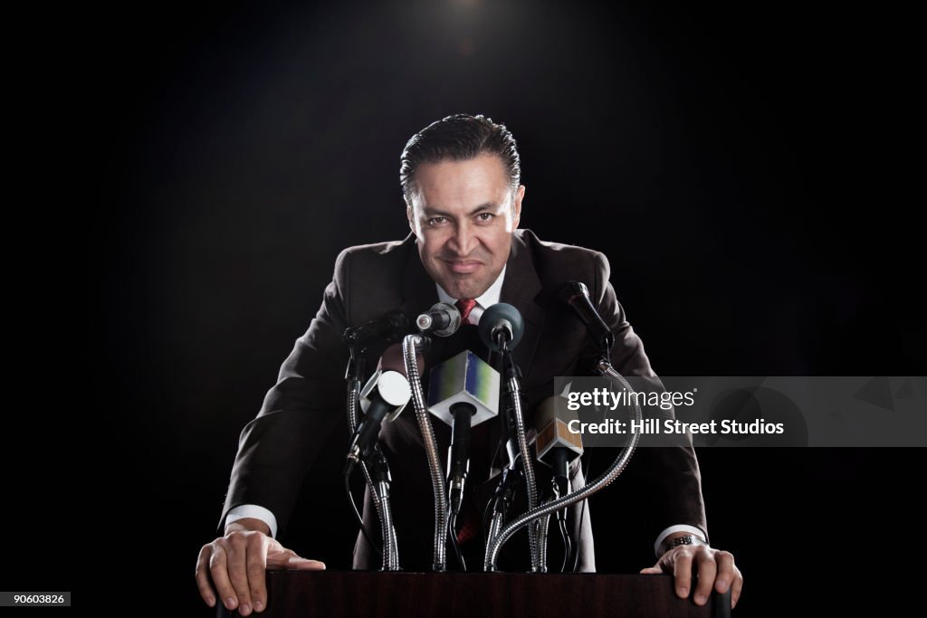 Hispanic man standing at podium with microphones
