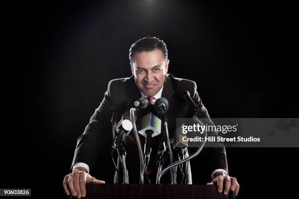 hispanic man standing at podium with microphones - arrogant man stock pictures, royalty-free photos & images