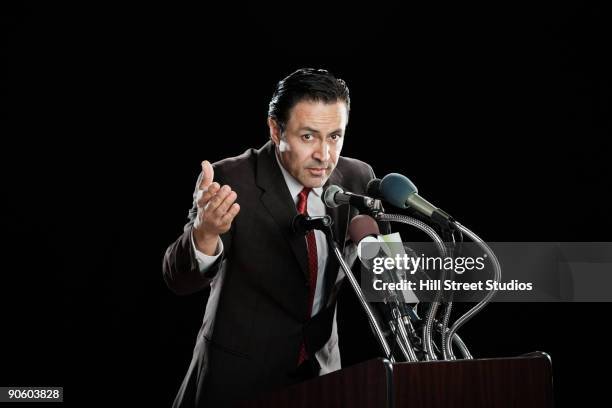 hispanic man gesturing at podium with microphones - politician speaking stock pictures, royalty-free photos & images