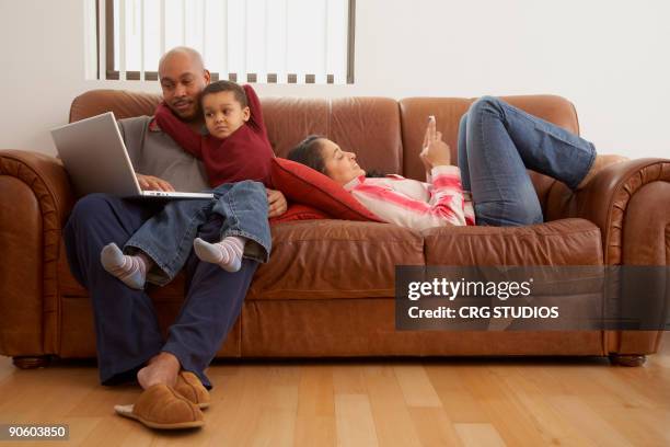 antiguan man using laptop in living room with family - dominican ethnicity stock pictures, royalty-free photos & images