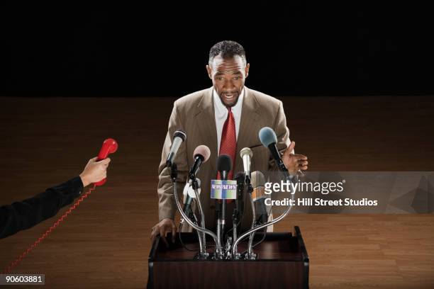 man with red phone interrupting african man at podium with microphones - mike storen stockfoto's en -beelden