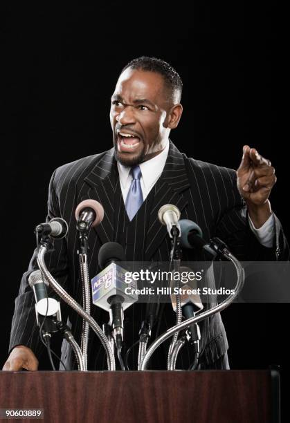 angry african man gesturing at podium with microphones - black politician stock pictures, royalty-free photos & images