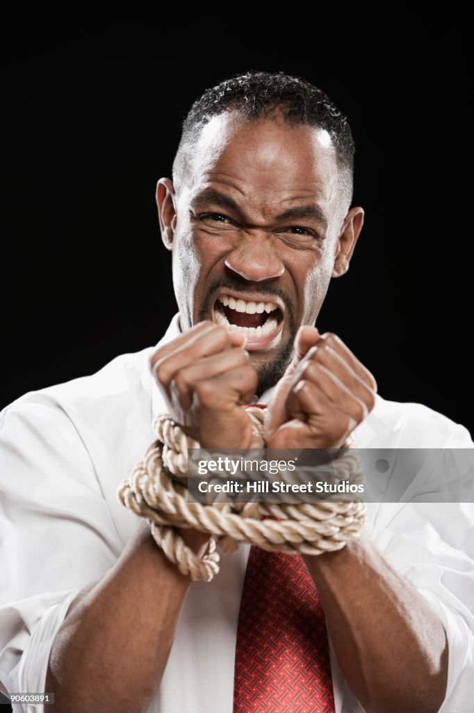 Angry African man with wrists bound by rope