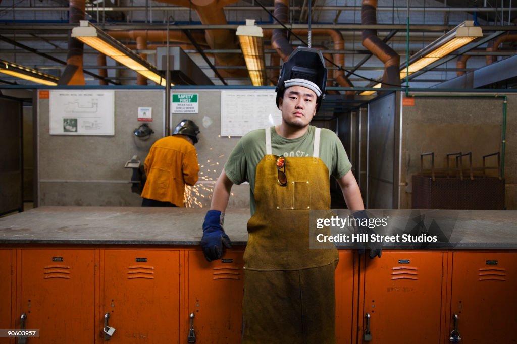 Mixed race welder leaning against lockers