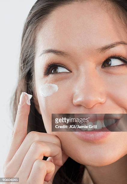 mixed race woman applying cream under eyes - beauty studio moisturisers stock pictures, royalty-free photos & images