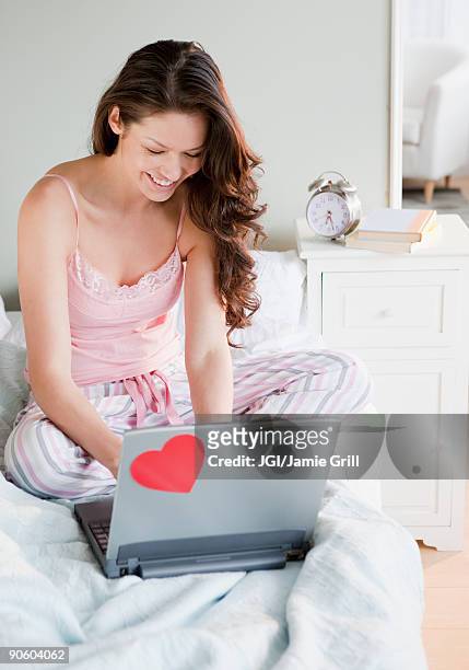 mixed race woman using laptop on bed - dating app foto e immagini stock