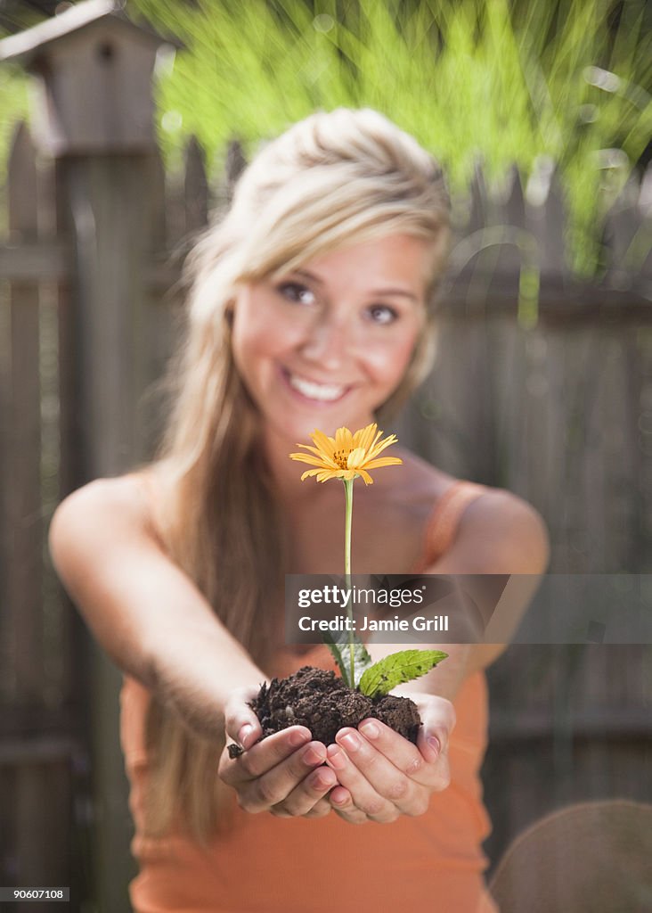 Young woman holding flower in dirt