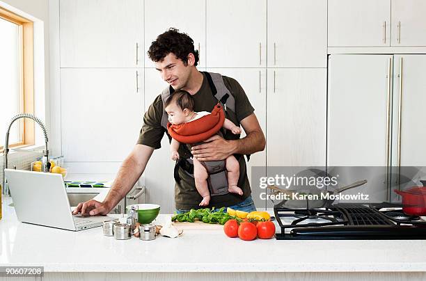 man cooking while holding baby - portabebés fotografías e imágenes de stock