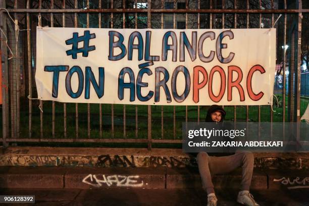 Demonstrator sits by a hashtag banner reading "Balance ton Aeroporc", playing on words between airport and pig, refering to the #MeToo and...