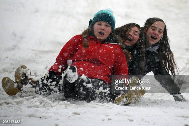 Three girls smile while sledding down a hill at Dorothea Dix Park during a snow storm on January 17, 2018 in Raleigh, North Carolina. North Carolina...