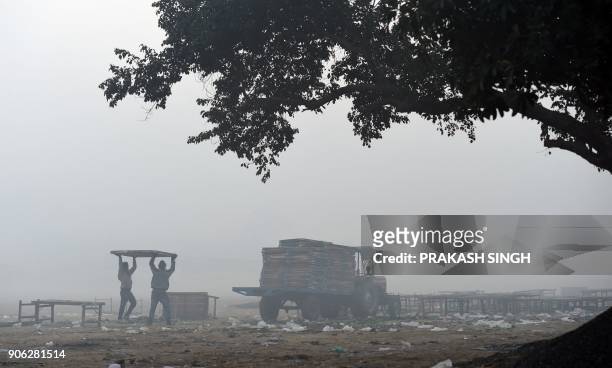 Indian labourers load foldable tables on a tractor trolly on a cold foggy morning on the outskirts of New Delhi on January 18, 2018.