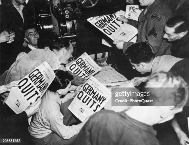 Allied soldiers and others read copies of the Stars and Stripes military newspaper, off the press , that announces Germany's surrender in World War...