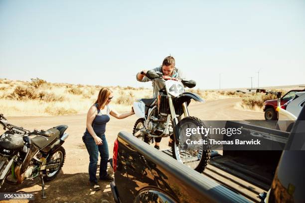 women taking dirt bike out of bed of truck before desert ride - motorcross foto e immagini stock