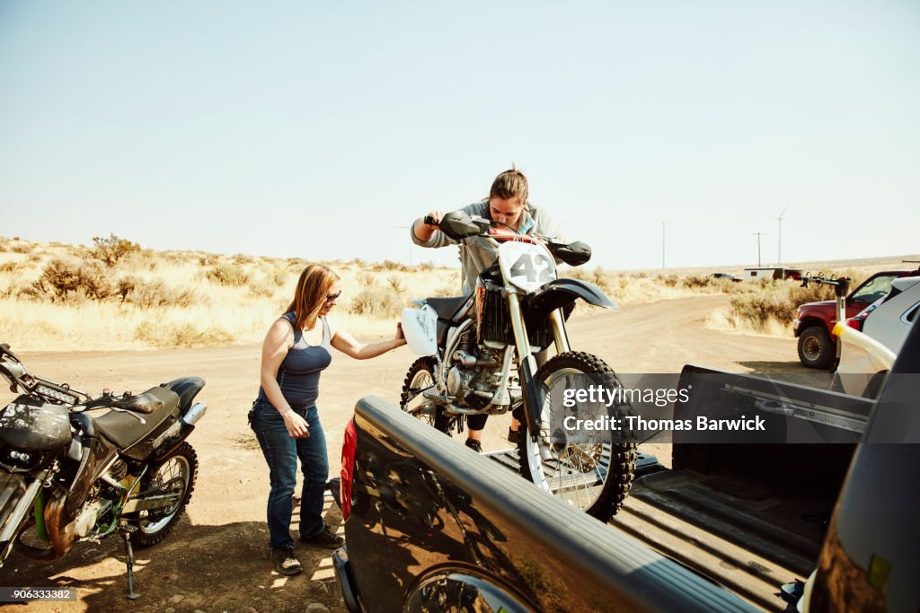 Women taking dirt bike out of bed of truck before desert ride