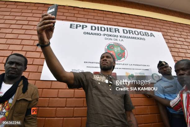 Ivory Coast's football star Didier Drogba takes a picture with his smartphone in front of a sign of the Primary School Didier Drogba during its...
