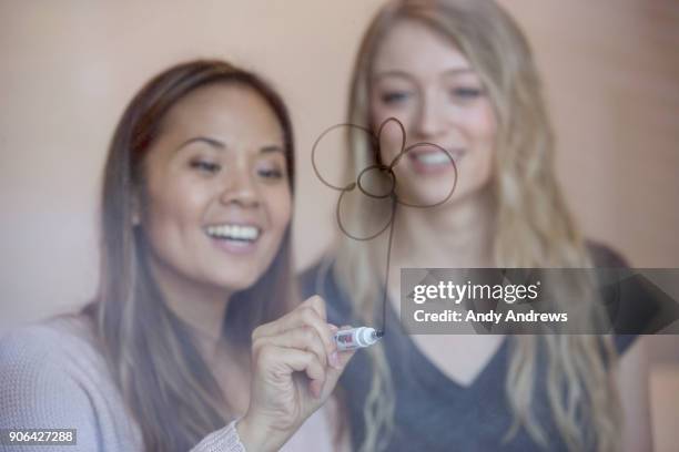 young women writing with a marker on glass - andy andrews stockfoto's en -beelden