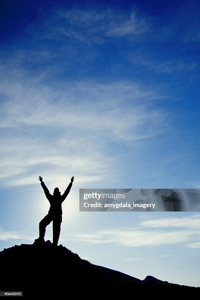 Hiker silhouette arms raised big sky clouds landscape