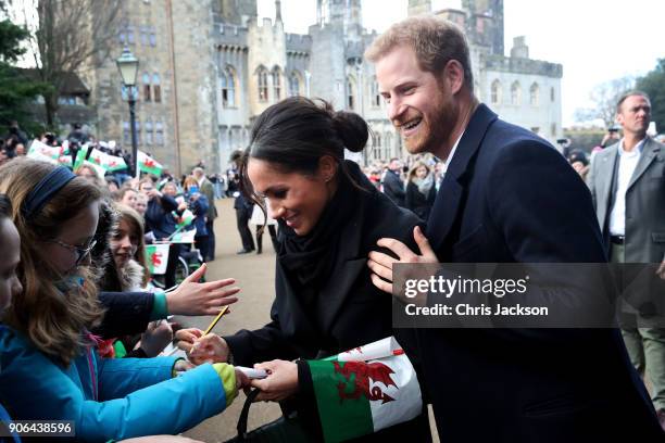 Prince Harry and his fiancee Meghan Markle sign autographs and shake hands with children as they arrive to a walkabout at Cardiff Castle on January...