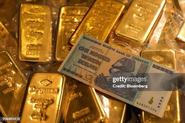 Zimbabwean one hundred trillion dollar note, worth one U.S. Dollar, sits on a pile of one kilogram bars of gold at the Sharps Pixley Ltd. Showroom in...