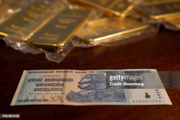 Zimbabwean one hundred trillion dollar note, worth one U.S. Dollar, sits next to one kilogram bars of gold at the Sharps Pixley Ltd. Showroom in this...
