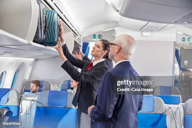 flight attendant helping businessman place luggage in overhead compartment on airplane - platzieren stock-fotos und bilder