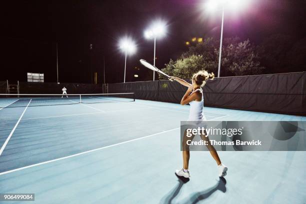 female tennis player hitting return while practicing on outdoor court at night - usa court stock-fotos und bilder