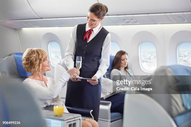 flight attendant serving champagne to woman in first class on airplane - stewardess stock-fotos und bilder
