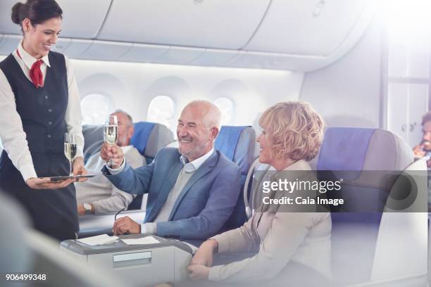 flight attendant serving champagne to mature couple in first class on airplane - first class champagne stock pictures, royalty-free photos & images