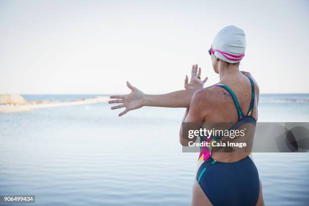 female open water swimmer stretching arm and shoulder at ocean - over the shoulder view stockfoto's en -beelden