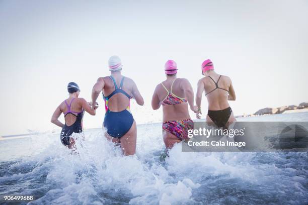 Female open water swimmers running and splashing in ocean surf