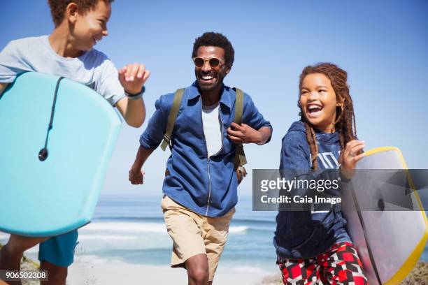 Happy father and children with boogie boards running on sunny summer beach