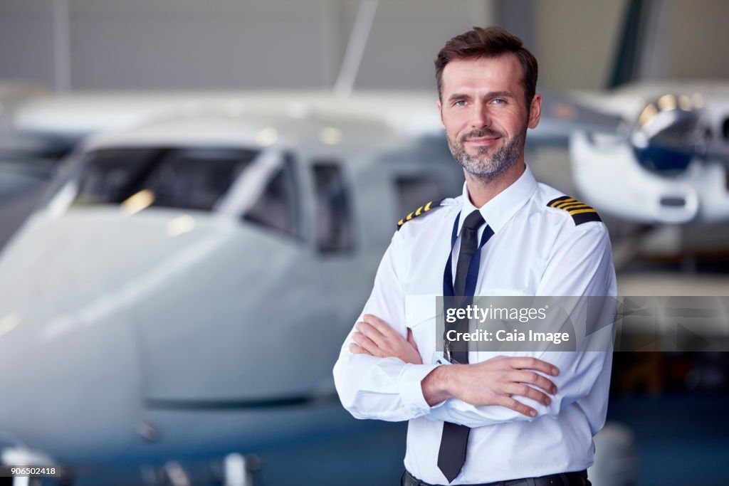 Portrait confident male pilot standing near airplane in hangar
