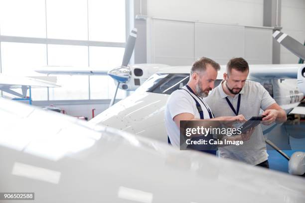 male mechanic engineers using digital tablet near airplane in hangar - digital techniques ストックフォトと画像