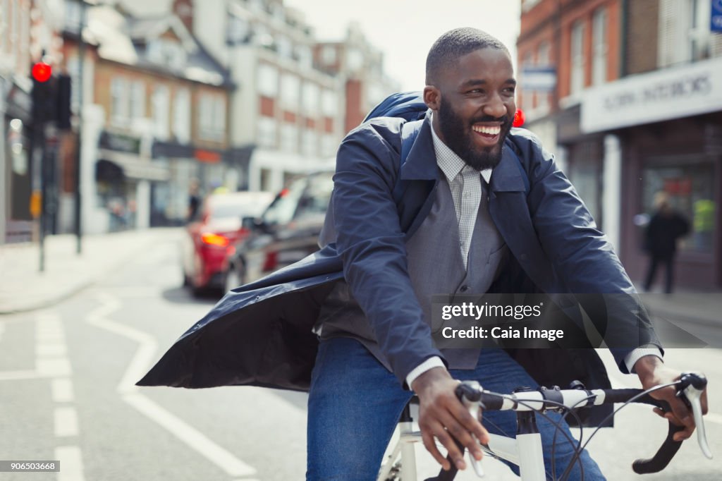 Smiling young businessman commuting, riding bicycle on sunny urban street