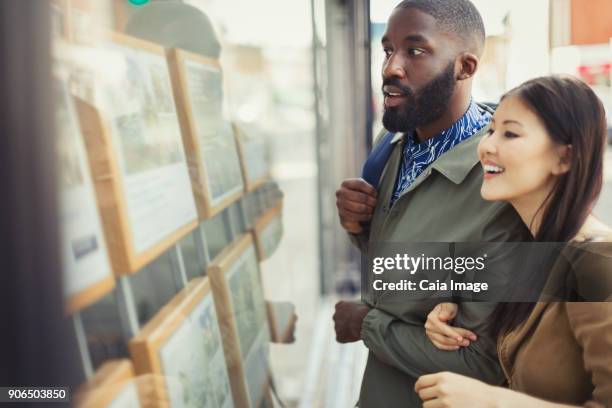 young couple browsing real estate listings at storefront - ethnic millennial real estate stockfoto's en -beelden