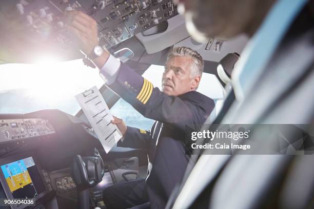 male pilot with clipboard preparing, adjusting instruments in airplane cockpit - flight-instruments stockfoto's en -beelden