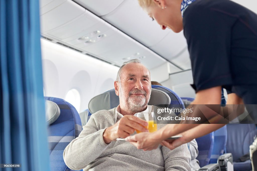 Flight attendant serving orange juice to man on airplane