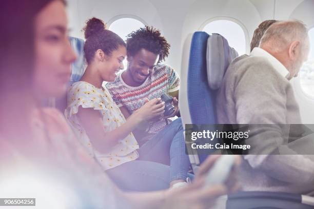 young couple looking at photos on digital camera on airplane - interracial wife photos stock-fotos und bilder